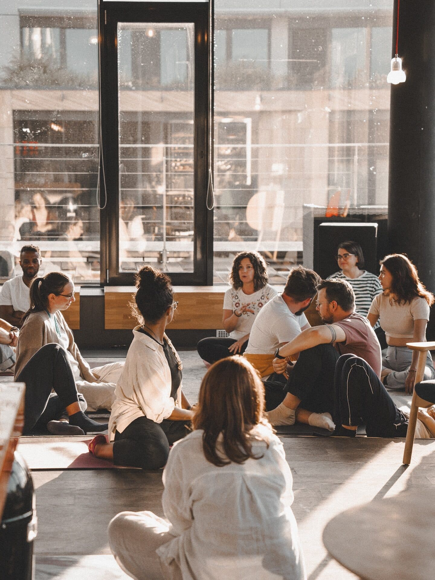 A group sitting on the floor of a sunlit studio before a breathwork session