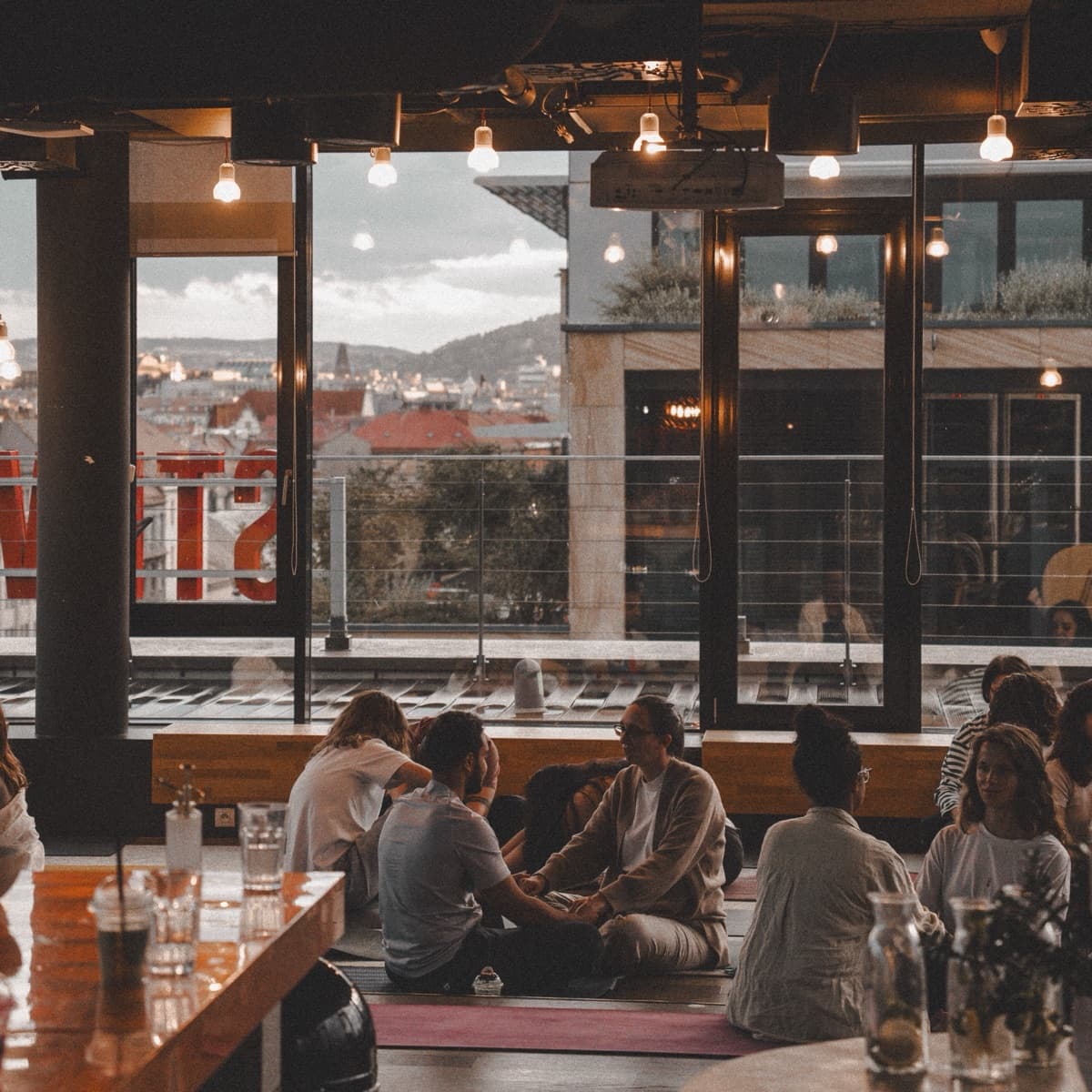 Pairs sitting on mats in a rooftop studio, with the Prague skyline behind the windows